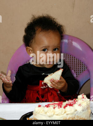 Un bambino di mangiare la sua torta come lei festeggia il suo primo compleanno Foto Stock