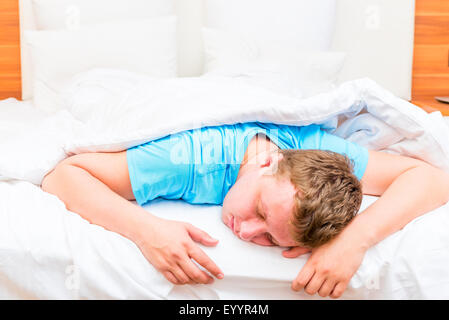 Uomo dormire su un letto bianco fogli Foto Stock