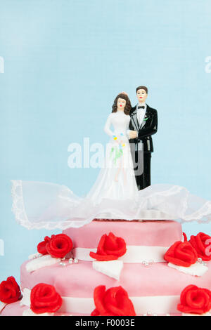 Rosa torta di nozze con rose rosse e la coppia in alto su sfondo blu Foto Stock