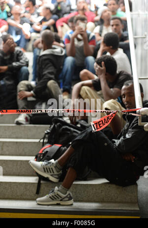 Rosenheim, Germania. 04 Ago, 2015. Un gruppo di rifugiati provenienti da vari paesi in attesa di essere registrati si siede su una rampa di scale alla stazione ferroviaria in Rosenheim, Germania, 04 agosto 2015. La polizia tedesca prelevati circa 150 rifugiati provenienti da vari paesi in un treno in arrivo da Verona. Dopo aver cercato e registrati hanno ricevuto un documento di identificazione presso un ufficio del tedesco della polizia federale e sono stati inviati al rifugiato struttura di accoglienza di Monaco dove essi possono chiedere asilo. Foto: ANDREAS GEBERT/dpa/Alamy Live News Foto Stock