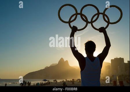 RIO DE JANEIRO, Brasile - 05 Marzo 2015: atleta detiene anelli olimpici sopra tramonto vista dello skyline della citta' di Ipanema Beach. Foto Stock