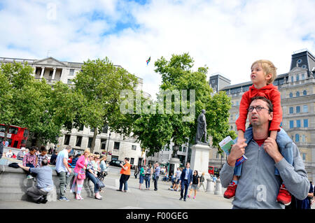 Londra, Inghilterra, Regno Unito. Ragazzo seduto su di suo padre a spalle in Trafalgar Square Foto Stock