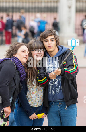 I turisti posano per un autoritratto usando un telefono cellulare e un bastone selfie fuori Buckingham Palace, London, Regno Unito. Foto Stock