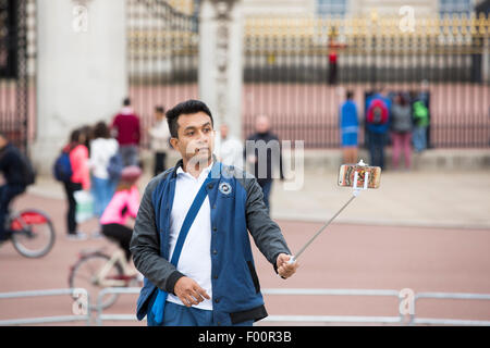 Tourist posare per un autoritratto usando un telefono cellulare e un bastone selfie fuori Buckingham Palace, London, Regno Unito. Foto Stock