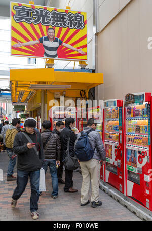 Giapponese uomini studio i telefoni cellulari e i distributori automatici in un vicolo in Akihabara Electric Town Foto Stock