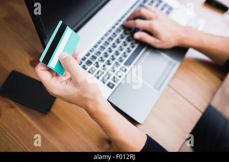 Uomo in possesso di una carta di credito e la digitazione. Shopping on-line su internet utilizzando un computer portatile Foto Stock