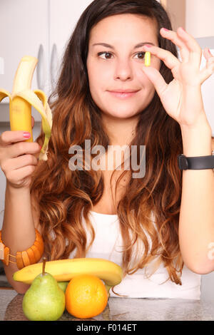 Una giovane donna tenendo un supplemento pillola in una mano e una banana nell'altro. Foto Stock