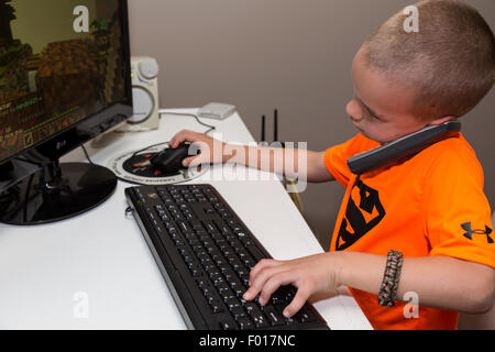 Il Multitasking inizia presto. Young Business Executive in formazione. Sette anni di vecchio ragazzo parla al telefono durante la riproduzione di video. Foto Stock