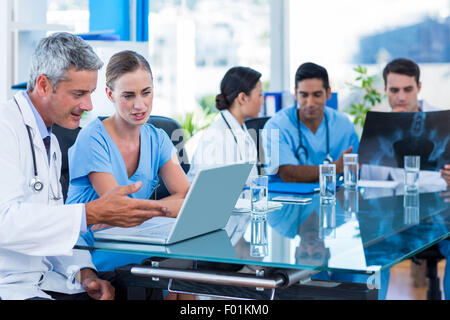 Medico e infermiere guardando il computer portatile con i colleghi dietro Foto Stock