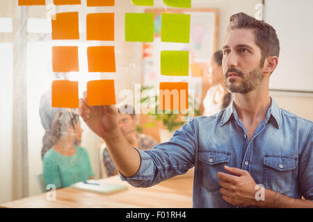 Imprenditore concentrato cercando il suo post sulla parete Foto Stock