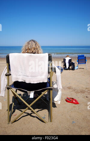 Donna rilassante in una sedia in riva al mare su di una spiaggia di sabbia Foto Stock