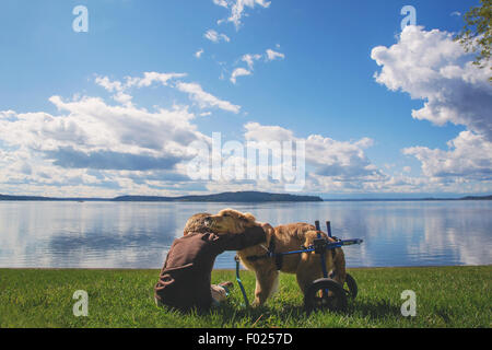 Ragazzo seduto su erba abbracciando un cane disabile, USA Foto Stock