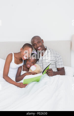 Ritratto di un bel giovane la lettura di un libro con la loro figlia a letto Foto Stock