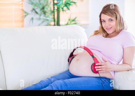 Sorridente donna incinta mettendo le cuffie sul suo ventre Foto Stock