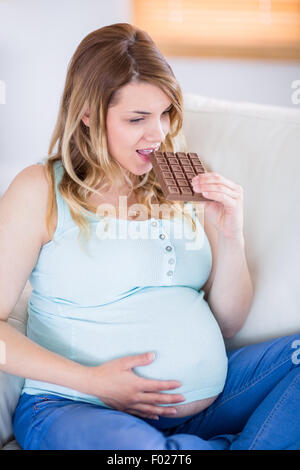 Bella donna incinta mangiare grandi barretta di cioccolato Foto Stock