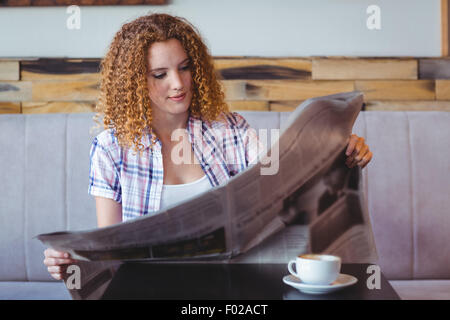 Bella capelli ricci ragazza avente tazza di caffè e un giornale di lettura Foto Stock