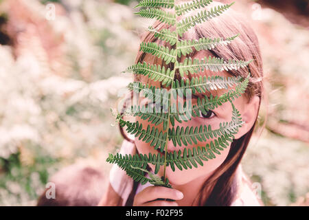 Ragazza nasconde il suo volto dietro una felce frond Foto Stock