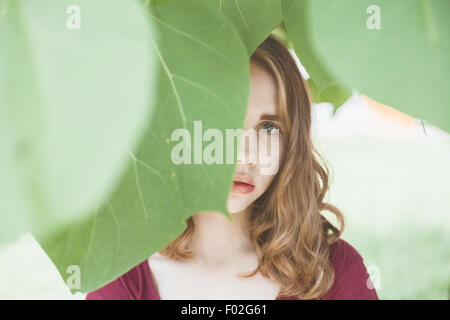 Ritratto di una giovane donna con la faccia oscurata da foglie Foto Stock