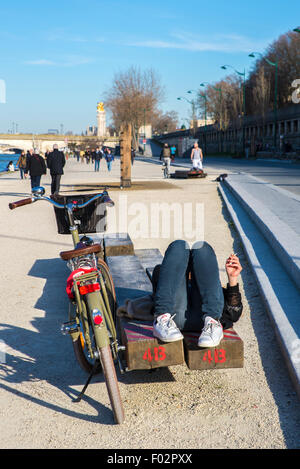 Donna sdraiata su un banco di lavoro sulle rive della Senna, Pont des invalides ponte dietro, Parigi Foto Stock
