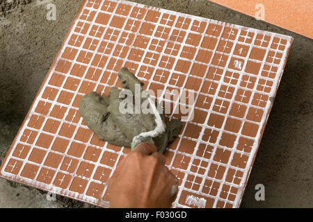 Un installatore al lavoro. Il legame della piastrella per pavimenti con piastrelle adesive e di riempimento. Foto Stock