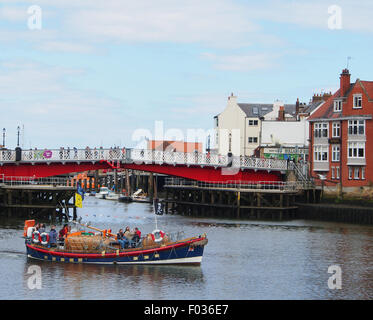 Scialuppa di salvataggio smantellata lasciando Whitby Harbour di prendere i turisti a bordo di una barca, con ponte rosso in background. Foto Stock