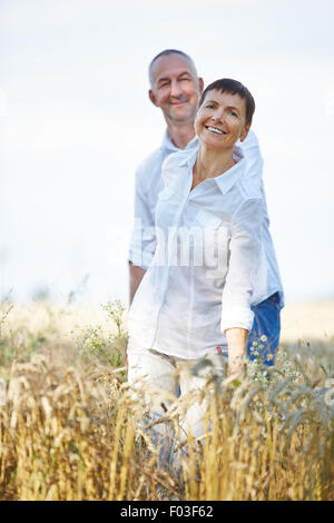 Felice coppia senior nel periodo delle vacanze estive a piedi attraverso un campo di grano Foto Stock