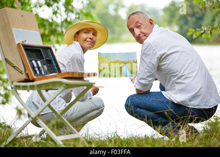 Felice coppia senior di pittura di apprendimento in natura in estate su un lago Foto Stock