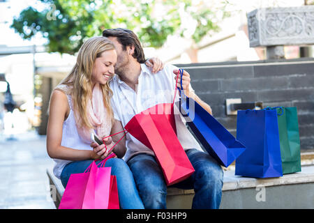 Uomo sorridente con borse per lo shopping a baciare la sua ragazza Foto Stock