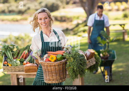 Sorridente agricoltore donna tenendo un cesto di ortaggi Foto Stock