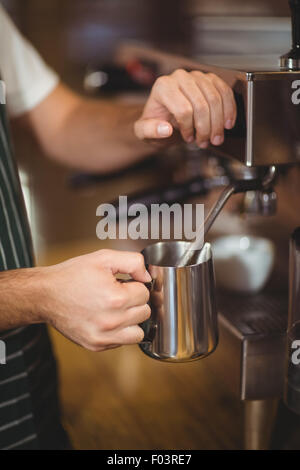 Barista latte di cottura a vapore in corrispondenza della macchina da caffè Foto Stock