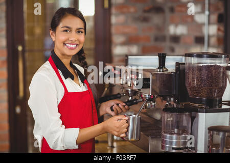 Sorridente barista latte di cottura a vapore in corrispondenza della macchina da caffè Foto Stock