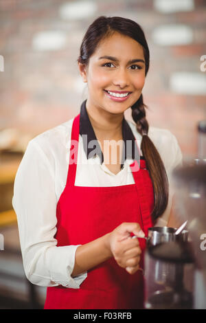 Sorridente barista latte di cottura a vapore in corrispondenza della macchina da caffè Foto Stock