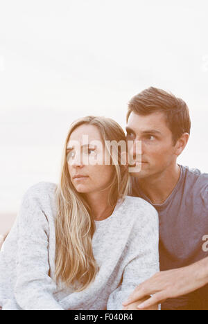 Un giovane seduto vicino a una spiaggia, un uomo e una donna con le braccia intorno a ogni altro e teste insieme. Foto Stock