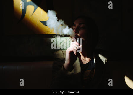 La ragazza si siede e fuma sigaretta elettronica Foto Stock