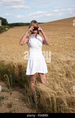 Donna che utilizza una fotocamera digitale per fotografare un campo di orzo nella campagna dell'Hampshire Southern England Regno Unito Foto Stock