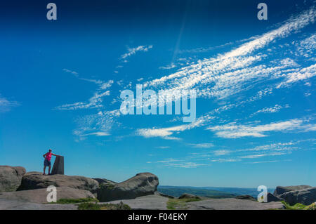 Figura solitaria a Trig, punto di triangolazione, sopra il bordo Stanage, Parco Nazionale di Peak District, Derbyshire, Inghilterra, Regno Unito. Cielo blu Foto Stock