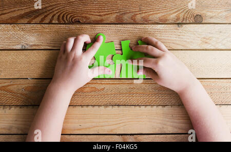 Immagine ritagliata delle mani di collegamento di due pezzi di un puzzle sul tavolo di legno Foto Stock