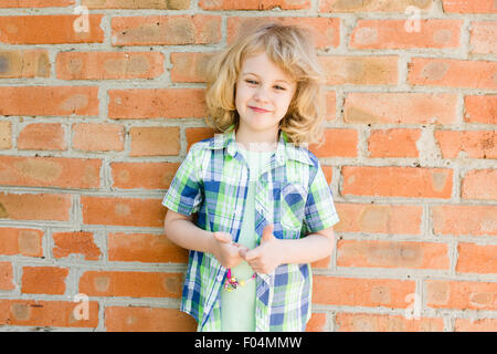 Ritratto di emozionale bambina abiti estivi all'aperto, muro di mattoni dietro Foto Stock