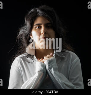 Latina teen in bianco maglietta a maniche lunghe in piedi di fronte a uno sfondo nero Foto Stock