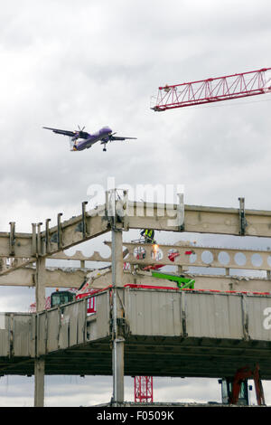 Flybe Bombardier Q400 twin a turboelica in atterraggio a City Airport London dietro di gru a torre galeoni a raggiungere lo sviluppo, Docklands Foto Stock