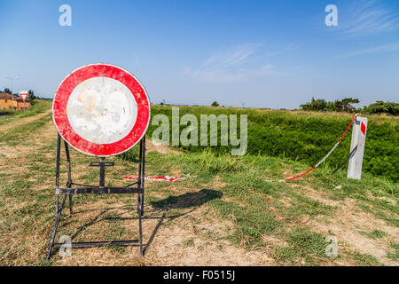 I cartelli stradali e strade di campagna - una sbiadita limite di velocità di 30 MPH segno a diventare un segno di proibire l'accesso al sentiero sulla sponda di un fiume Foto Stock