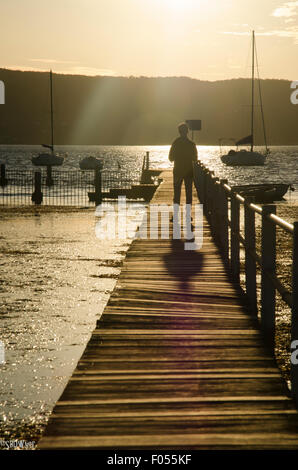 Un ragazzo (adolescente) camminando verso il tramonto su una stretta wharf Foto Stock