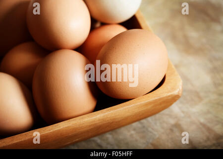 Uova di colore marrone nella ciotola di legno sul tavolo di legno Foto Stock