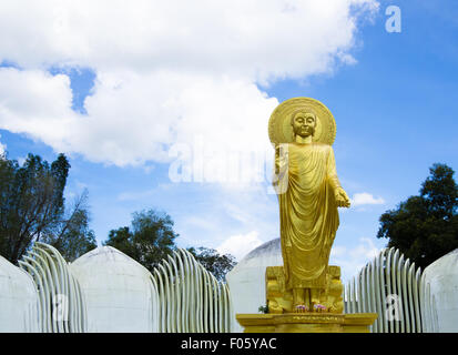 Golden Buddha alto permanente con il blu del cielo e alcune nuvole in background Foto Stock