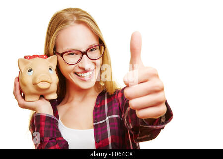 Sorridente donna felice con il salvadanaio tenendo il suo pollice in alto Foto Stock