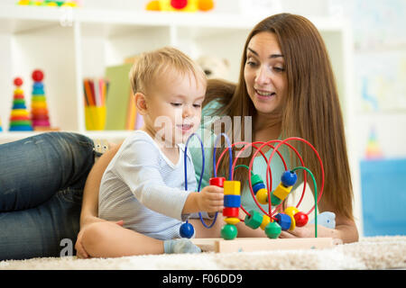 Ragazzo bambino gioca con il giocattolo educativo indoor. Felice madre guardando il suo smart figlio. Foto Stock