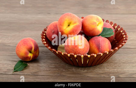 Pesche con cesto su sfondo di legno Foto Stock