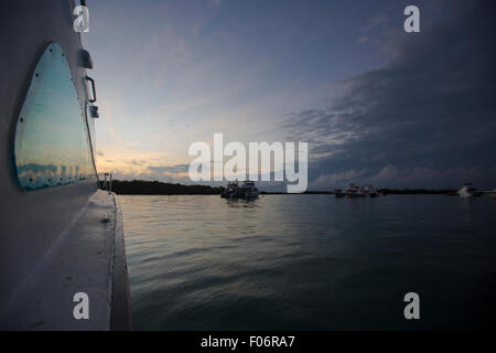 Sunrise blu con riflessi di luce nell'oceano da una crociera in barca con piccole imbarcazioni in background, Galapagos isola Foto Stock