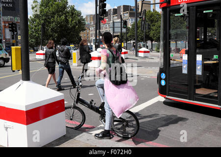 Una giovane donna su una bicicletta Brompton in attesa ad un semaforo accanto a un bus rosso a due piani nella parte est di Londra KATHY DEWITT Foto Stock