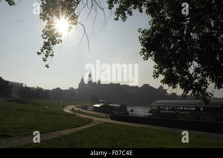 Blue sky di mattina presto, vista verso il colle di Wawel, il sole brilla attraverso il ramo di albero sul lato nord del fiume Vistola, Cracovia Foto Stock